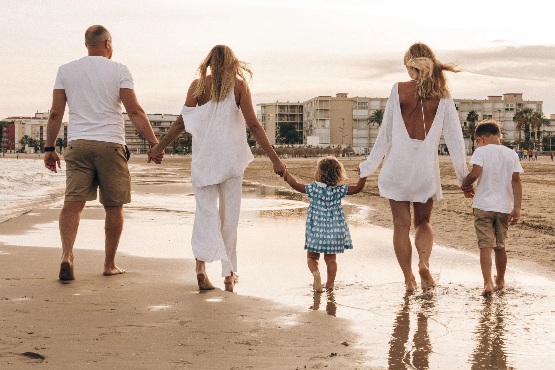 Family walking hand in hand along the beach at sunset, enjoying a warm summer day.